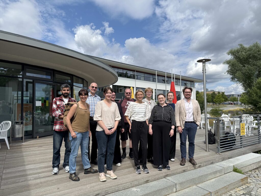 A group photo of the StoryMachine project team standing outside the Institute for Information Systems at Hof University of Applied Sciences during their first in-person meeting in July 2025